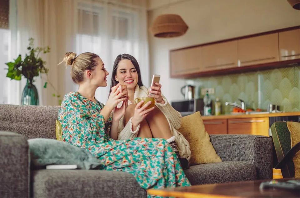 Two women looking at a smartphone on a sofa