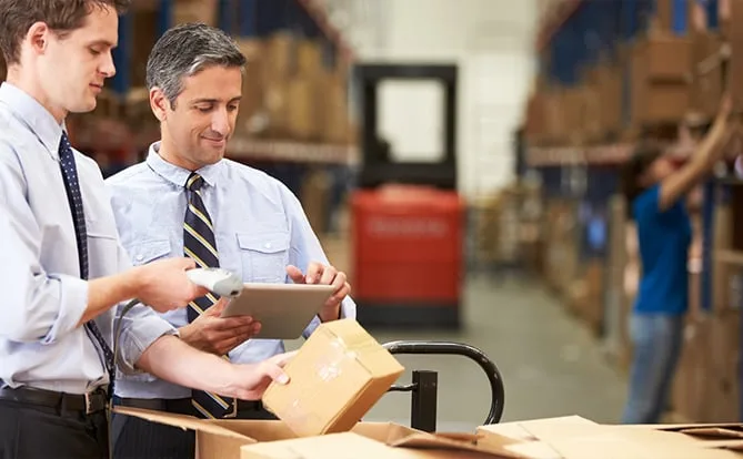 Two warehouse workers reviewing a tablet beside packaged goods