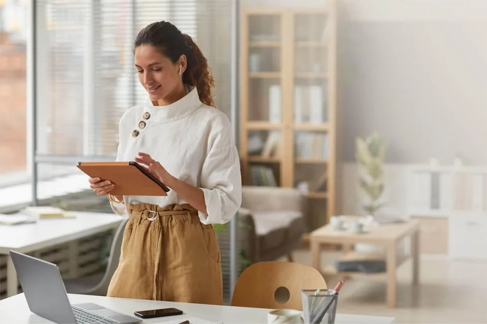 Woman reading a tablet beside a laptop